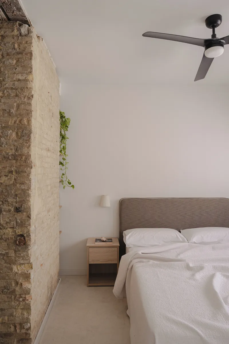 Bedroom with exposed brick wall and ceiling fan above a timber bed frame