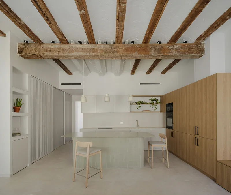 Kitchen with exposed timber ceiling beams, island with two stools, and white and wood cabinetry
