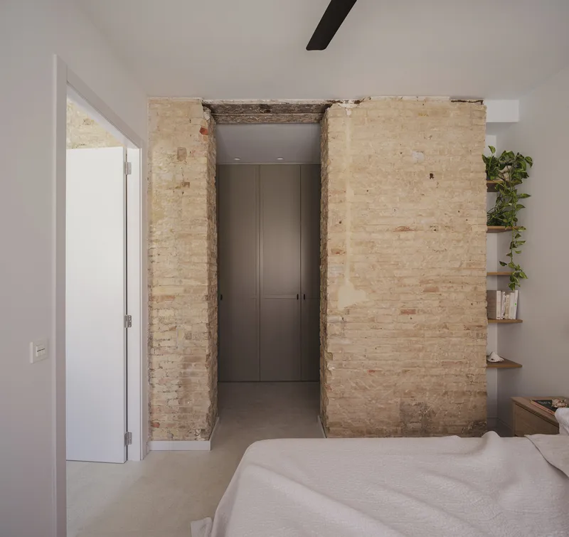Bedroom with exposed brick wall opening framing a doorway and floating shelves with trailing plants