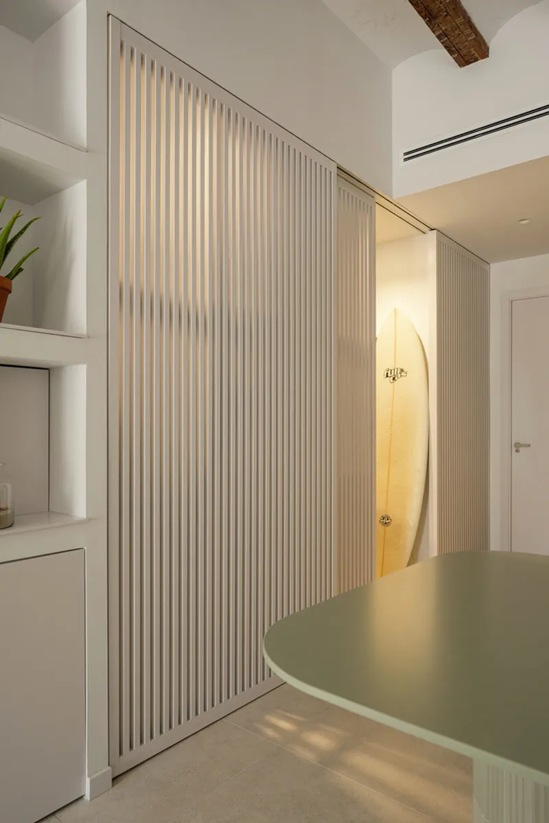 Sliding fluted panel revealing illuminated bathroom alcove behind kitchen counter at dusk