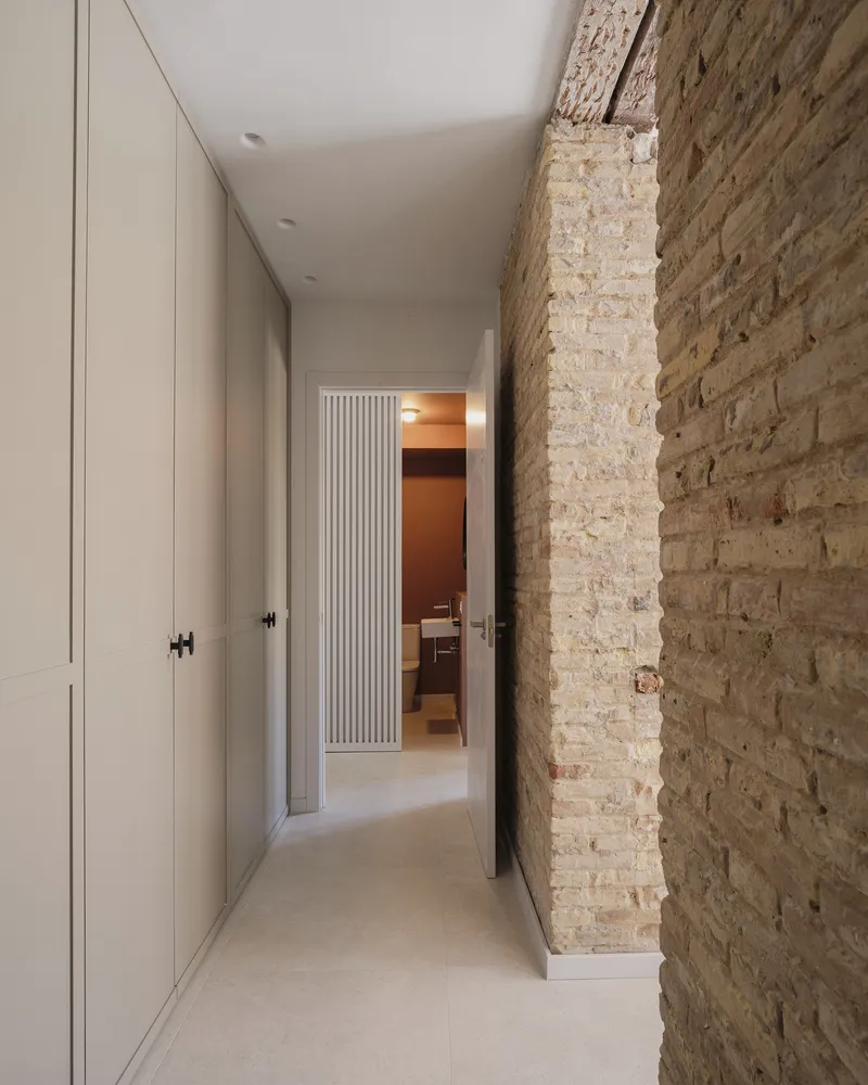 Narrow hallway with white cabinetry and exposed weathered brick wall leading toward fluted doorway