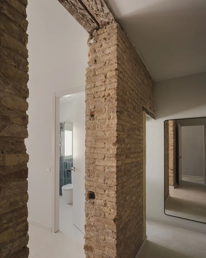 Exposed brick pillar with remnant openings beside doorway to bathroom in white interior