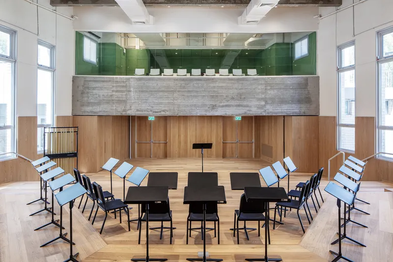 Orchestra rehearsal space with music stands arranged in rows beneath green glass upper balcony