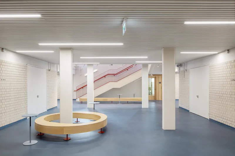 Lobby with white columns, curved timber bench seating, and red staircase visible in background