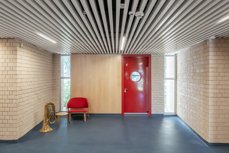 Entry vestibule with radiating slatted ceiling, red door with porthole window, and cream brick walls