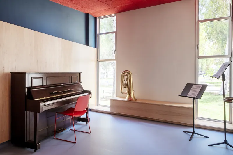 Music room with upright piano, built-in timber bench, music stand, and tall windows overlooking greenery