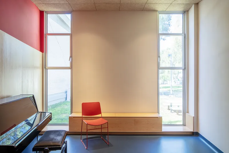 Practice room with red chair on timber bench seat flanked by full-height windows