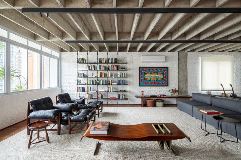 Living room with exposed concrete beam ceiling, painted brick walls and floor-to-ceiling windows facing adjacent buildings