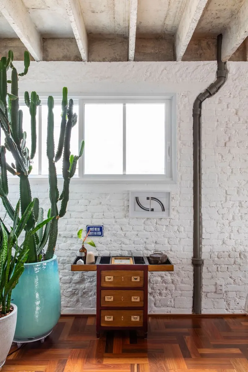 Workspace corner with painted brick walls, exposed conduit, potted cactus and herringbone wood flooring