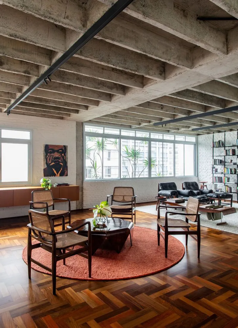 Open living area with cane-back chairs on a rust-colored circular rug under exposed concrete joists