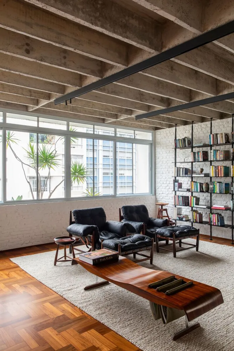 Seating area with leather lounge chairs and low coffee table beneath concrete beam ceiling with metal track