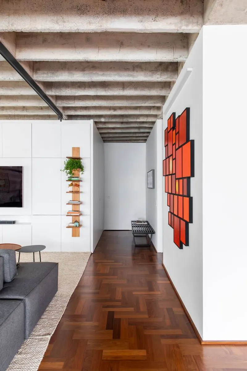 Hallway view showing herringbone wood flooring leading beneath exposed concrete joists