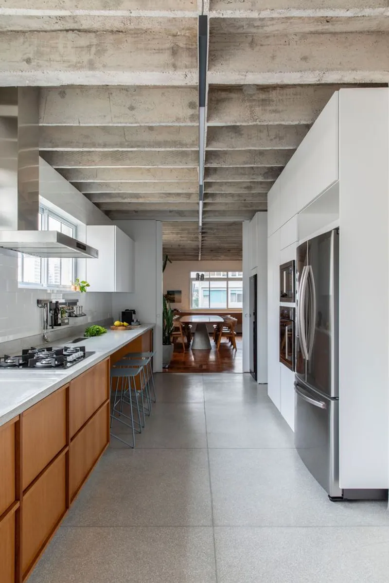 Galley kitchen with exposed concrete ceiling and view through to dining area in natural light
