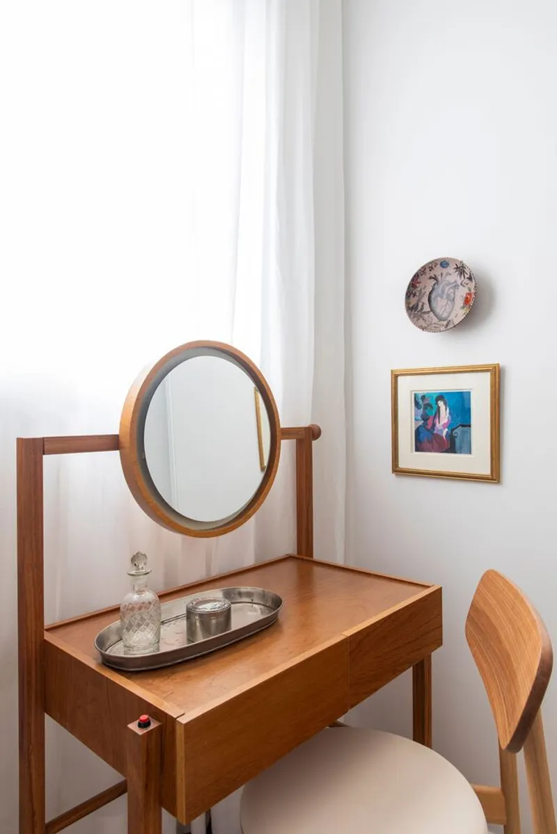 Timber vanity table with oval mirror against white wall beside window with sheer curtain