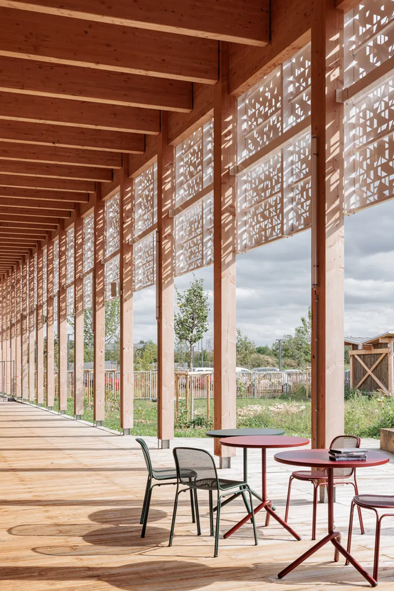 Covered timber walkway with perforated screen panels and scattered seating overlooking a meadow garden
