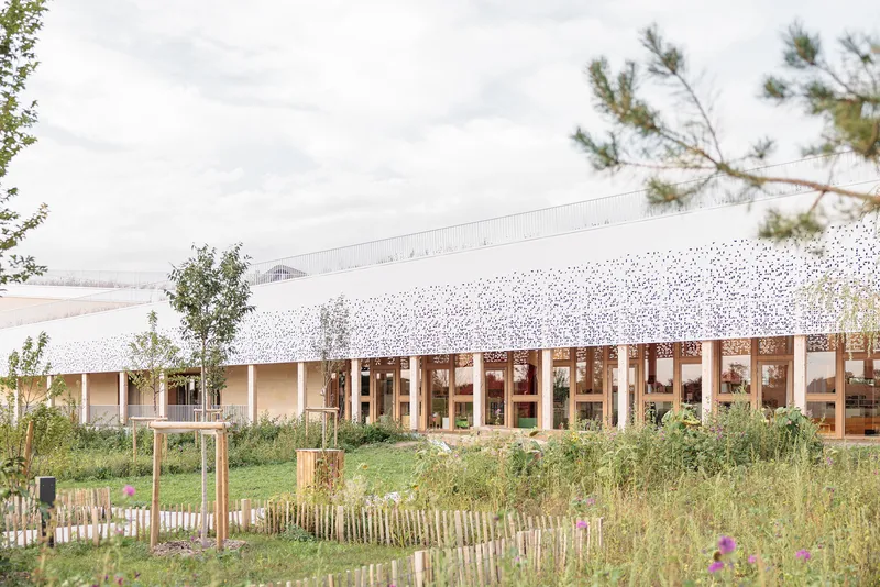 Perforated white facade with timber columns visible behind wildflower planting and overcast sky