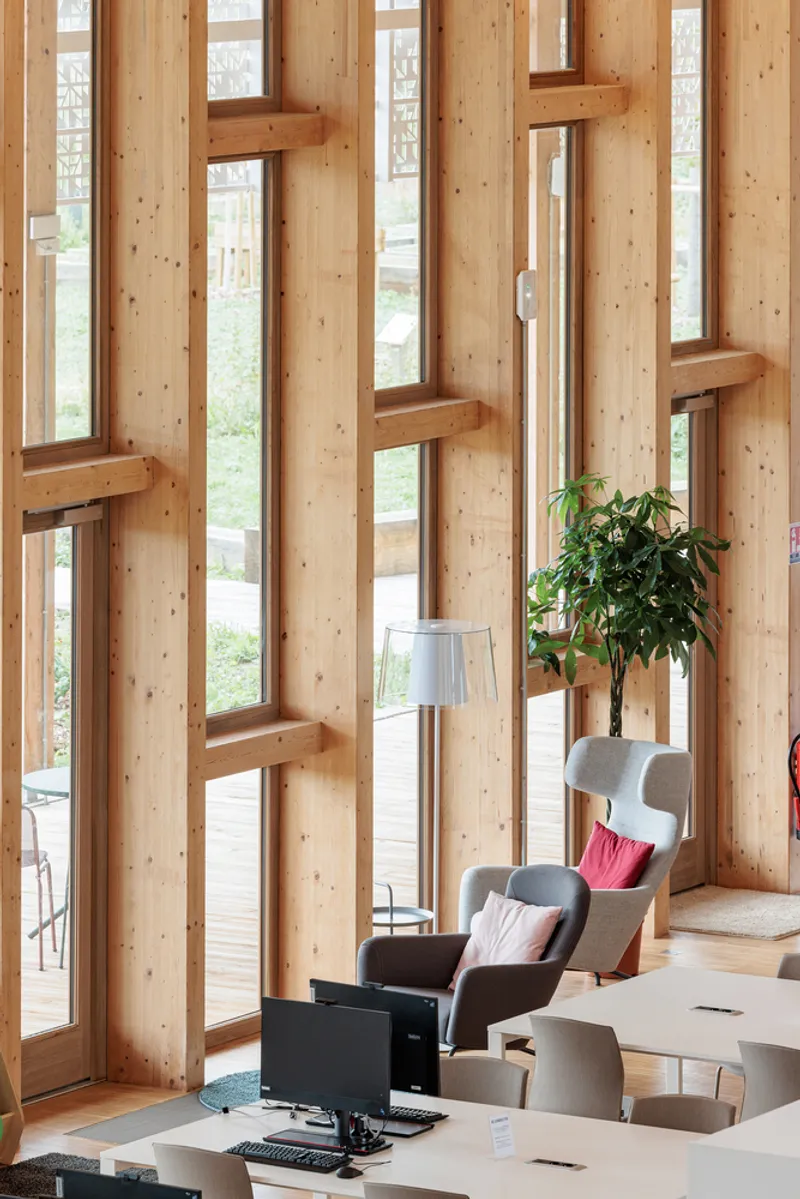 Interior timber wall with staggered vertical windows and reading chair beside a potted plant