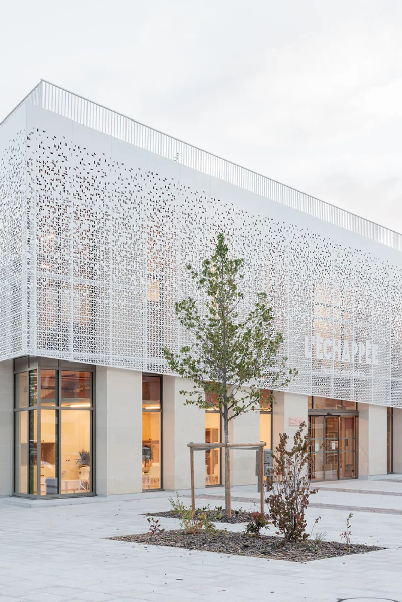 White perforated metal facade with planted courtyard trees at dusk beneath cloudy sky