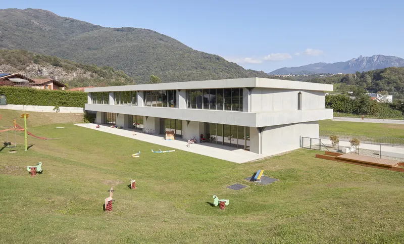 Two-storey horizontal volume with continuous glazing and cantilevered terrace overlooking a grassed play area with mountains beyond