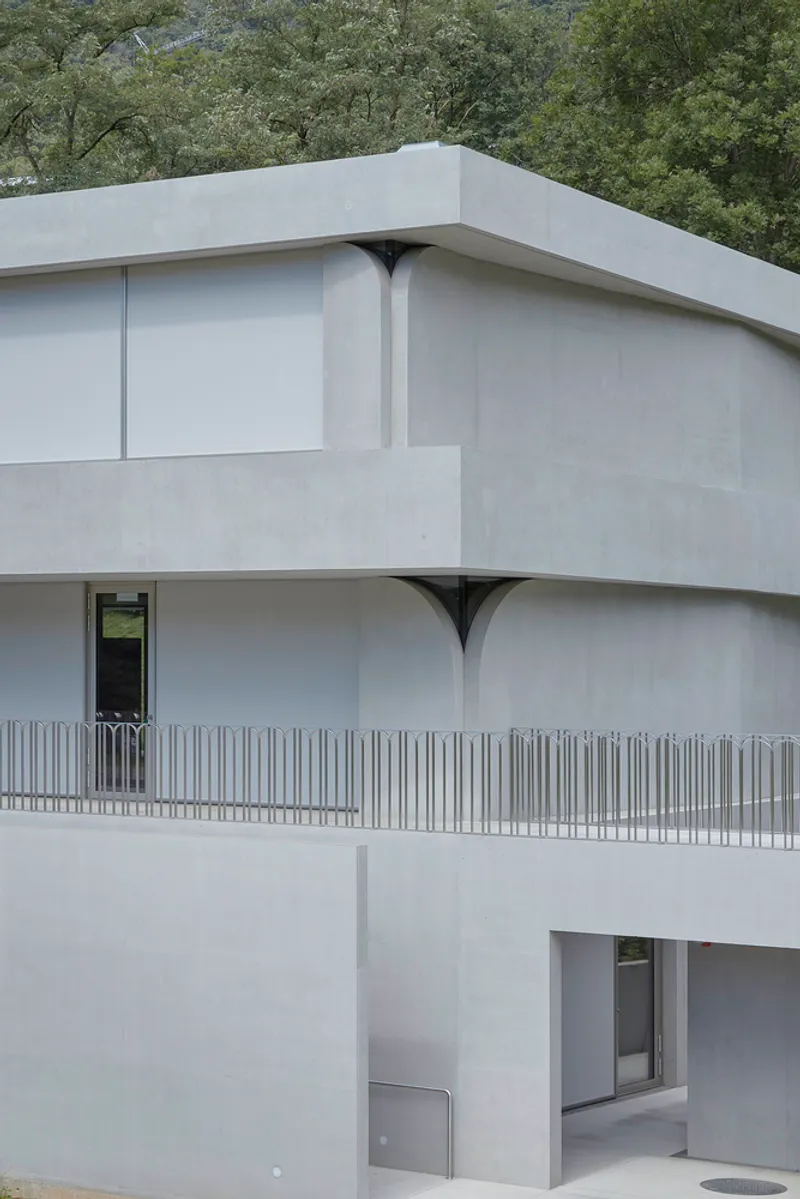 Corner detail of stacked concrete balconies with arched cutouts beneath the slab edges framed by trees