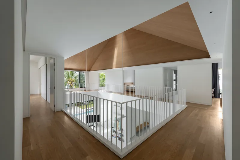 Upper-level corridor with white-painted balustrade wrapping the central void beneath an angled timber ceiling