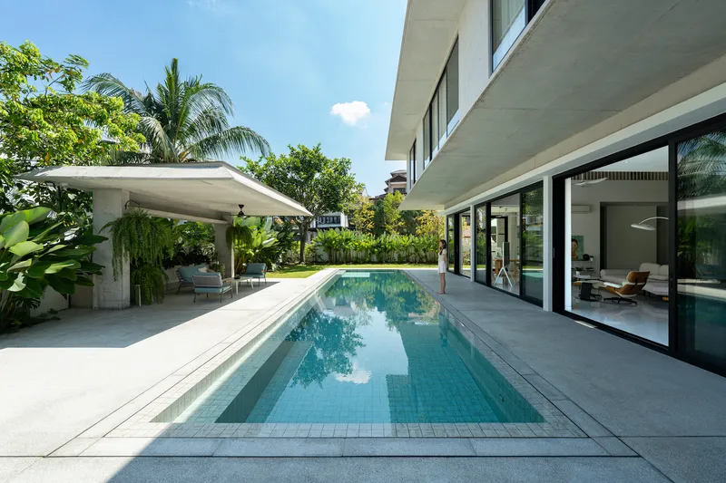Pool terrace with covered seating pavilion and glazed living spaces framed by palms and tropical planting