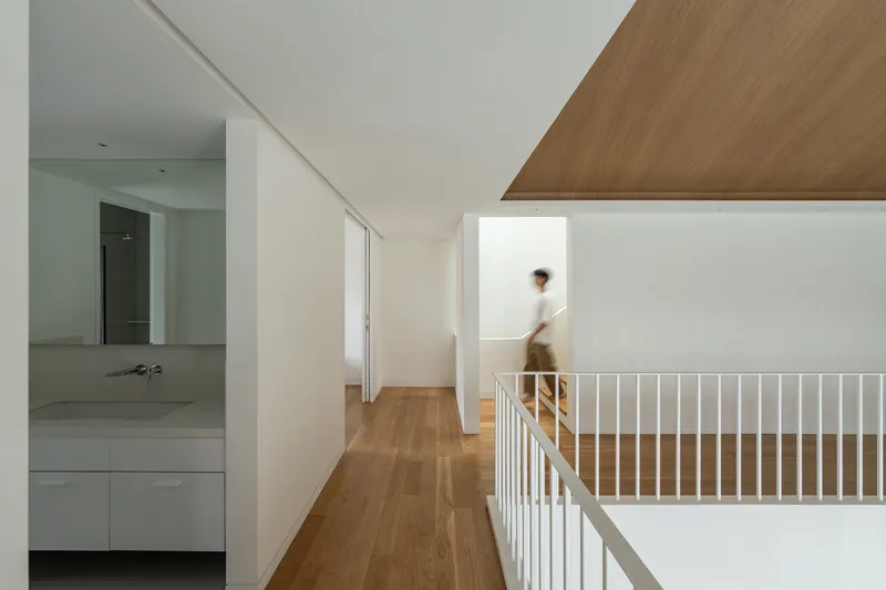 Upper hallway with white balustrade and timber flooring where a figure walks beneath an angled wood ceiling