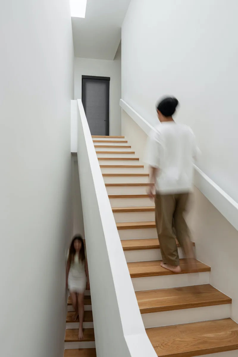 Timber staircase with white walls where two figures pass on different landings in motion blur
