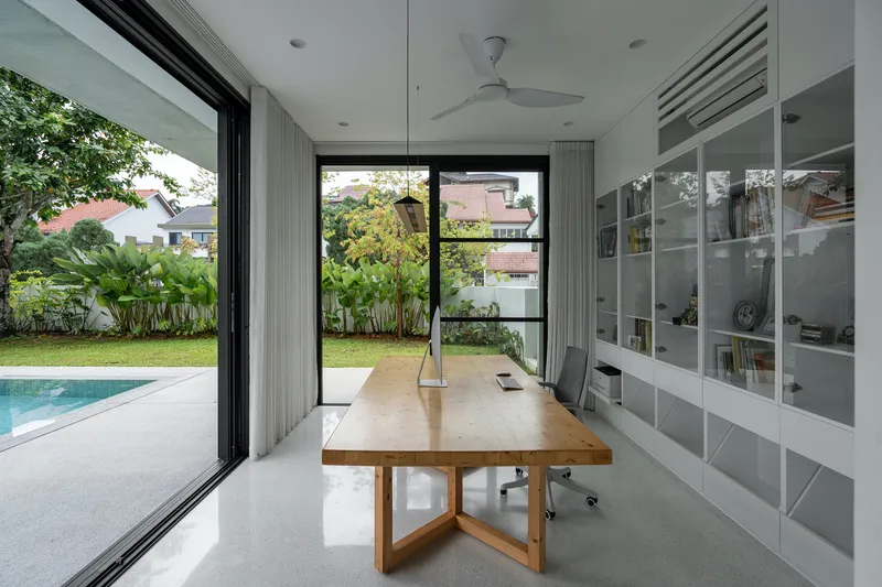 Dining room with timber table opening to lawn and pool through floor-to-ceiling glazed sliding doors