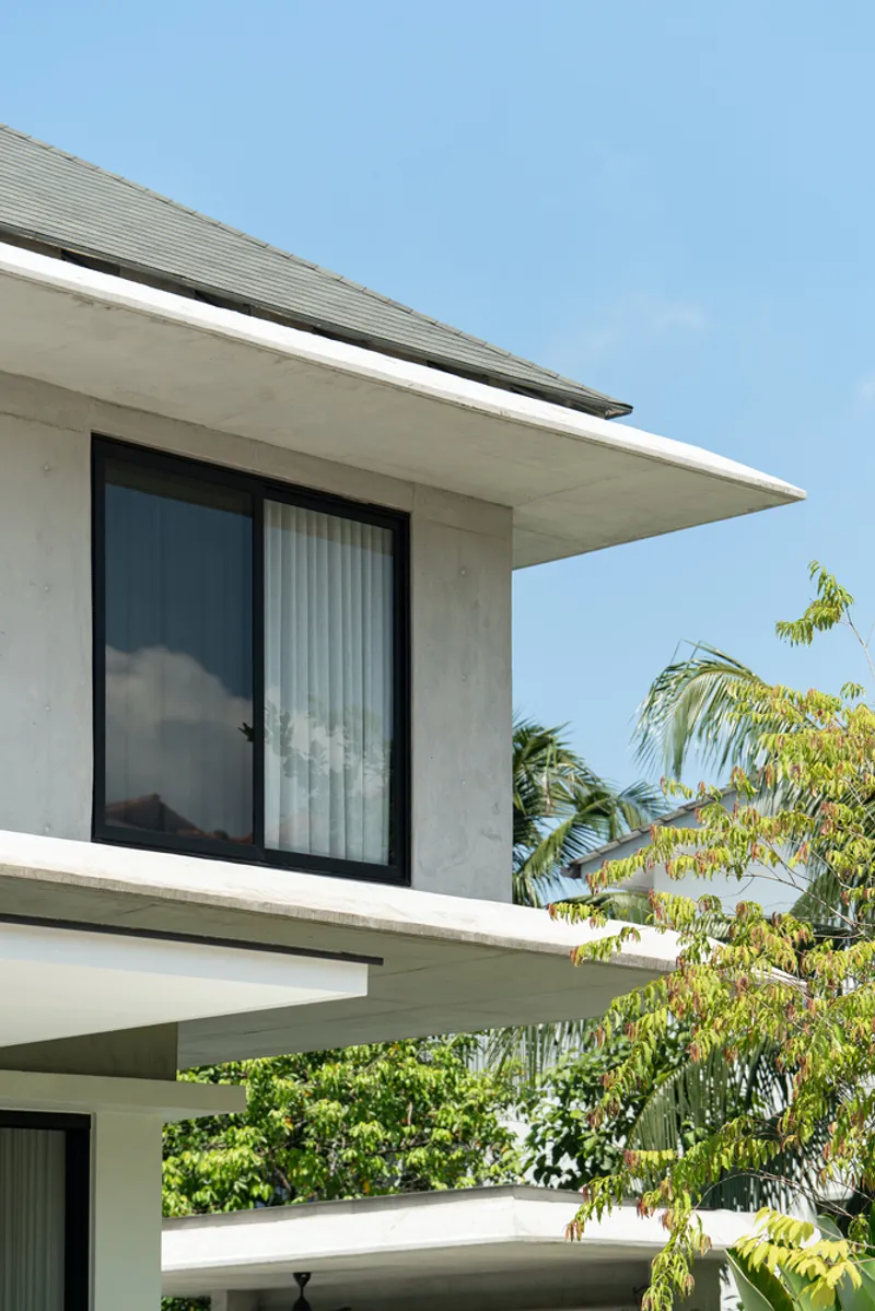 Concrete overhang with sliding glass doors and tiled roof above palm trees under clear sky