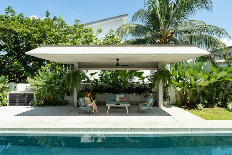 Poolside pavilion with a curved concrete canopy sheltering lounge furniture and lush tropical planting