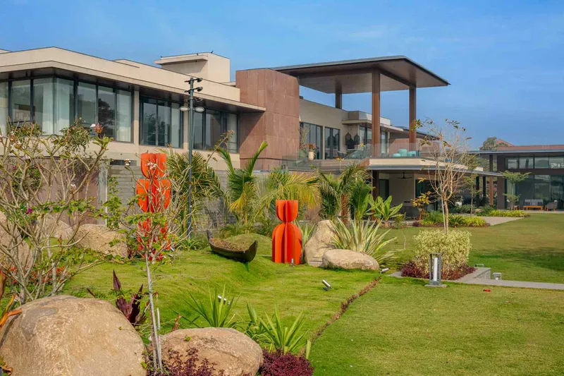 Garden view showing sculptural planters and red art piece among palm trees and boulders on a lawn