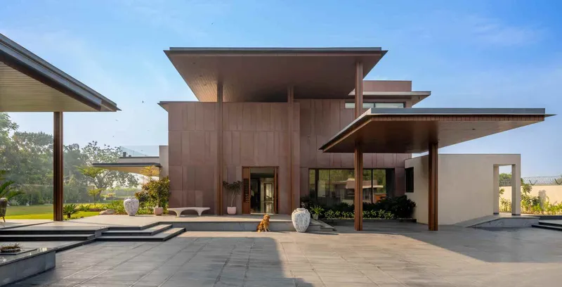 Entry courtyard with layered cantilevered roofs and sandstone tile cladding beneath a clearing sky