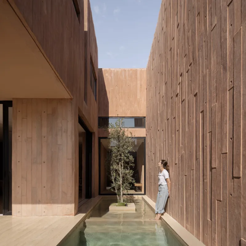 Exterior courtyard with shallow pool flanked by vertical timber walls and a woman standing at the edge