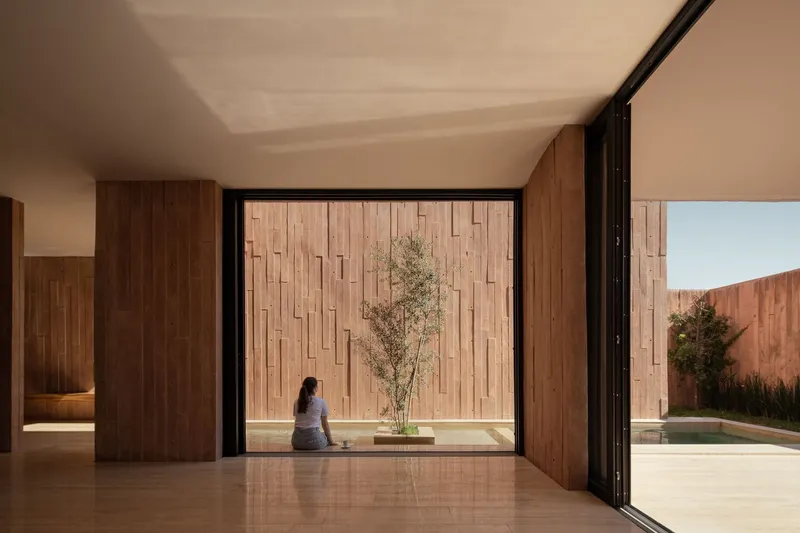 Open living space with floor-to-ceiling glazing overlooking a courtyard with a woman seated on the threshold