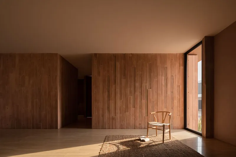 Timber-lined interior room with a single chair on a woven rug in afternoon sunlight