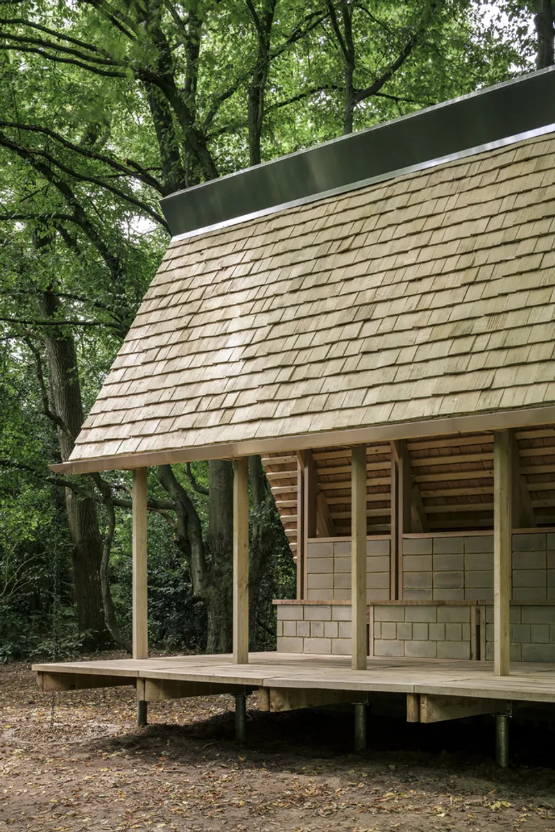 Elevated timber pavilion with cedar shingle roof and slatted screens nestled among mature trees