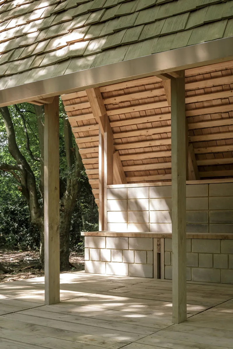 Detail of the timber post and beam frame beneath the shingled eave with masonry wall beyond