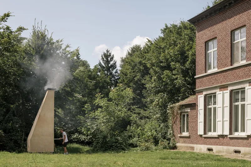 Tapered outdoor oven with smoking chimney beside a brick residence on a lawn