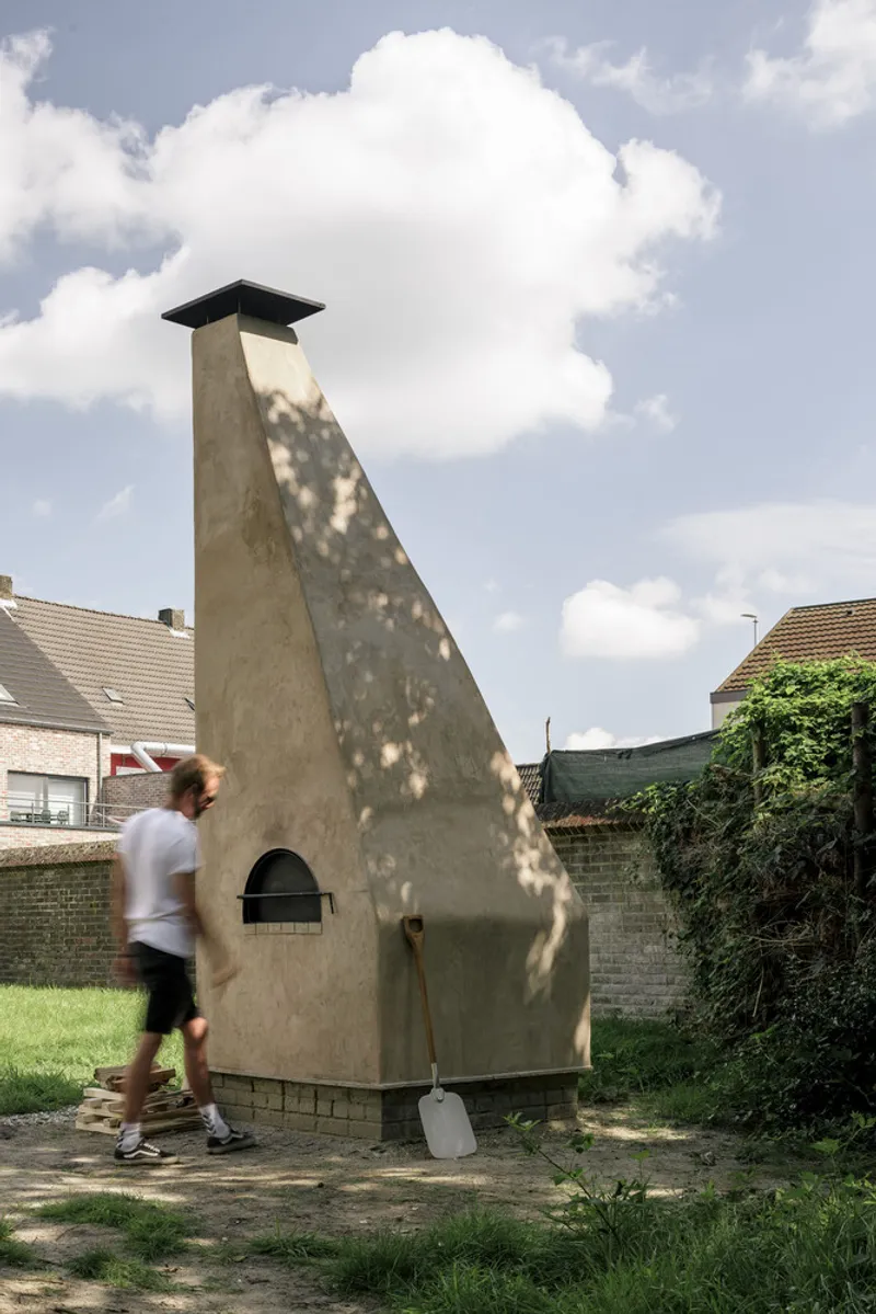 Freestanding pyramidal oven with arched opening as a person walks past in a garden