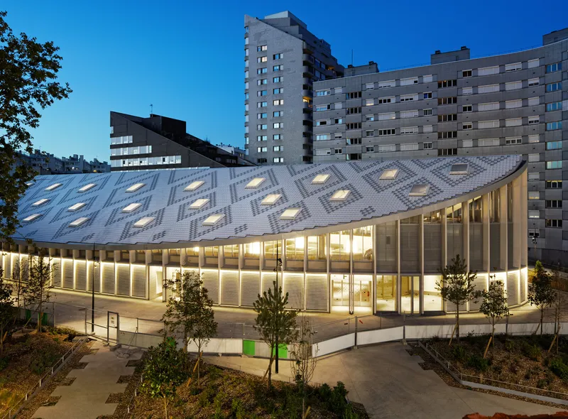 Night view of the illuminated glazed perimeter and patterned roof with diamond-shaped skylights at dusk