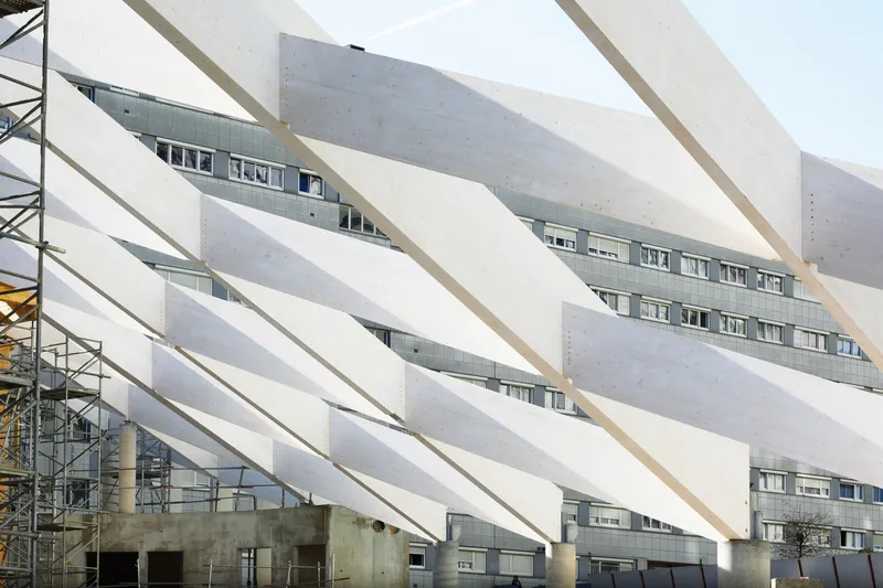 Layered white structural beams wrapping the facade with a construction crane visible at left