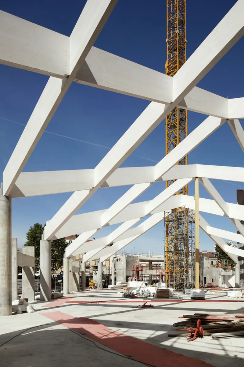 White laminated timber arches under construction against a clear blue sky with a crane tower rising between them