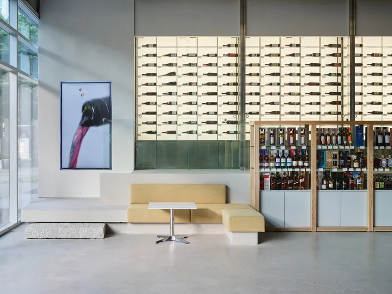 Yellow upholstered bench seating beneath vertical wine display with timber frames and digital screen on wall