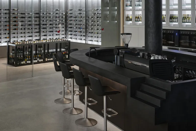 Black espresso bar with swivel stools facing illuminated wine storage wall and timber framed display shelving