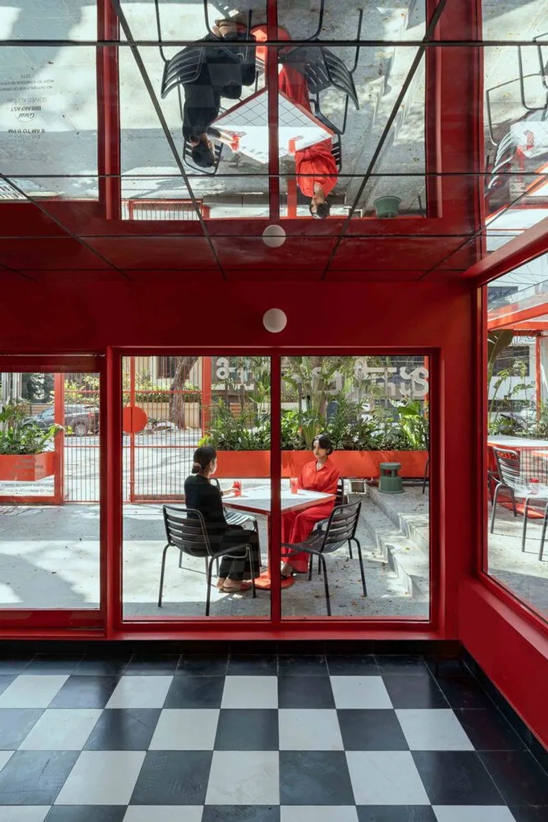 Interior view through red steel framing to outdoor seating area with person at table and chequered floor