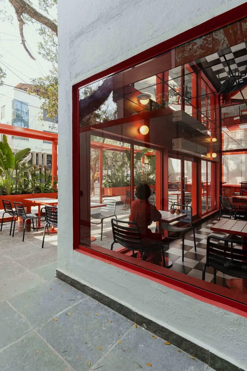 Red steel frame facade opening to a courtyard where a person sits at a table