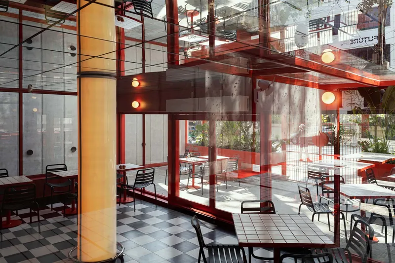 Interior view through glass walls showing red steel structure and checkered floor pattern in daylight