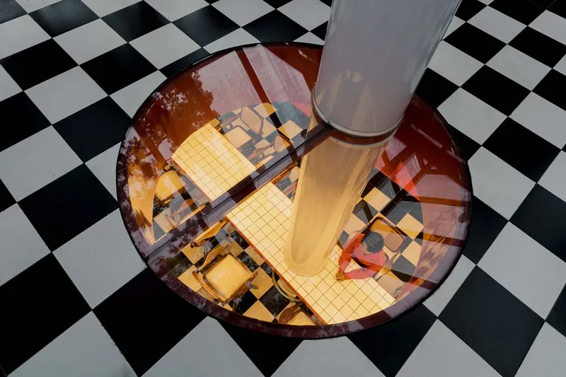 Circular floor opening with red glazing revealing seating area below, surrounded by checkered black and white tiles