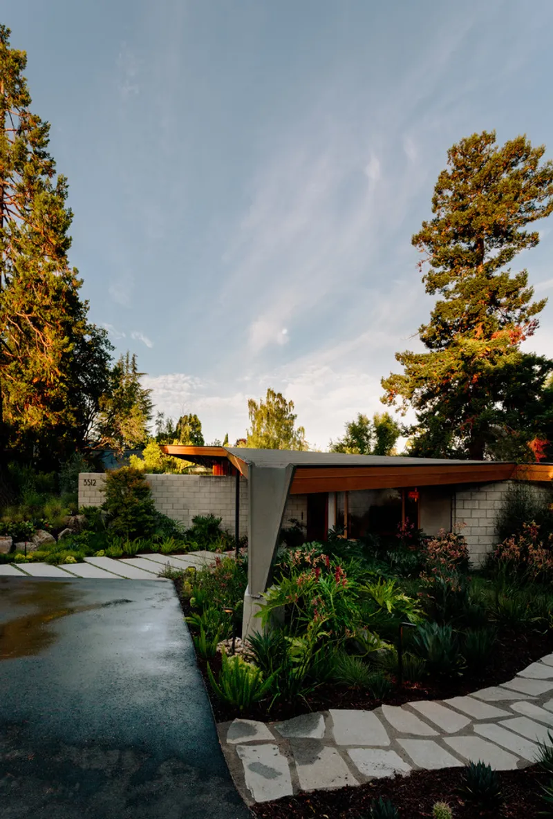 Curved concrete driveway with planted islands leading to a cantilevered entry canopy at twilight